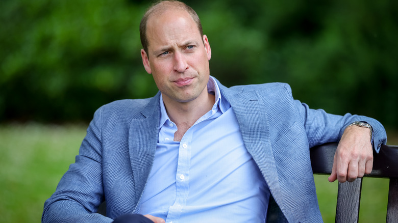 Prince William leaning back on a bench