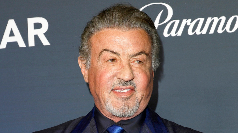 Sylvester Stallone smiling in a dark blue suit at AmFAR Las Vegas.