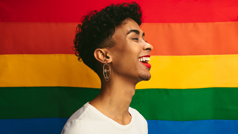 A person smiling in front of a pride flag