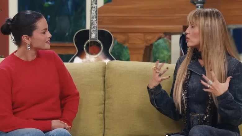 Selena Gomez and Miley Cyrus talk on a couch during the Hannah Montana 20th Anniversary