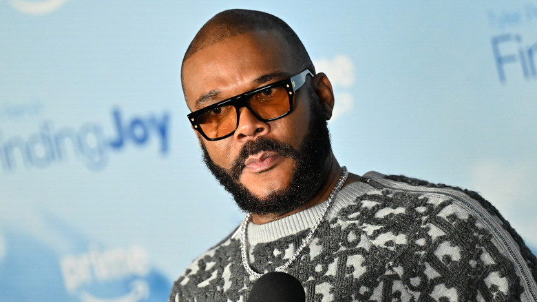 Tyler Perry holding a microphone while wearing sunglasses and a grey sweater