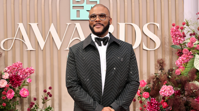 Tyler Perry posing at the BET Awards in a bowtie, glasses, and a sparkly black jacket