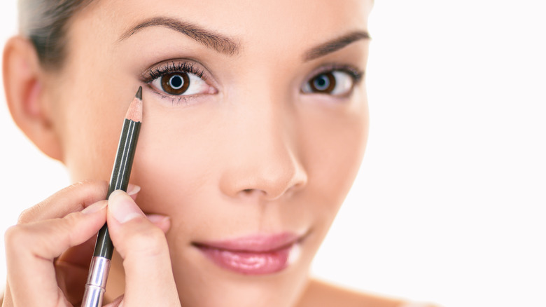 Woman holding eyeliner pencil up to her eye