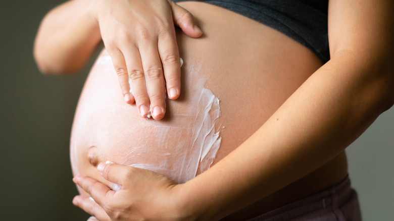 A person rubbing lotion on their pregnant belly 