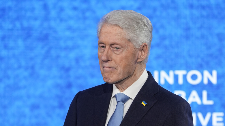 Bill Clinton pursing his lips in a navy suit with a light blue tie