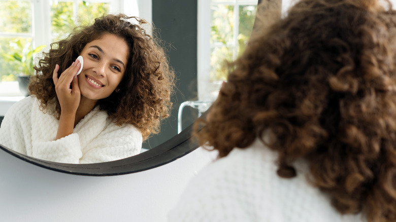 Woman washing face, looking in mirror