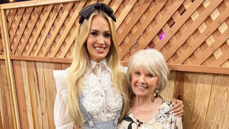 Carrie Underwood posing with mom Carole in front of a wooden lattice fence