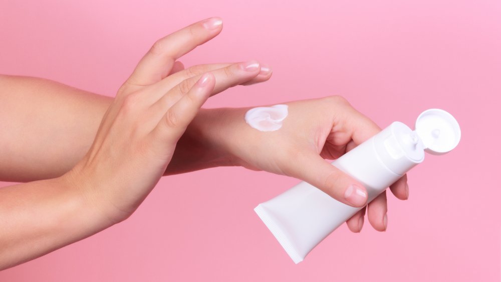 Woman applies clean beauty moisturizer on her skin. 