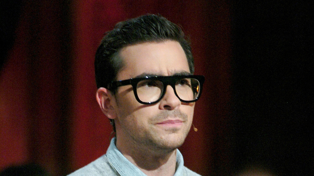 Dan Levy wearing glasses, looking off