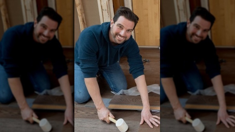 Scott McGillivray smiling while hitting a floor plank with a mallet