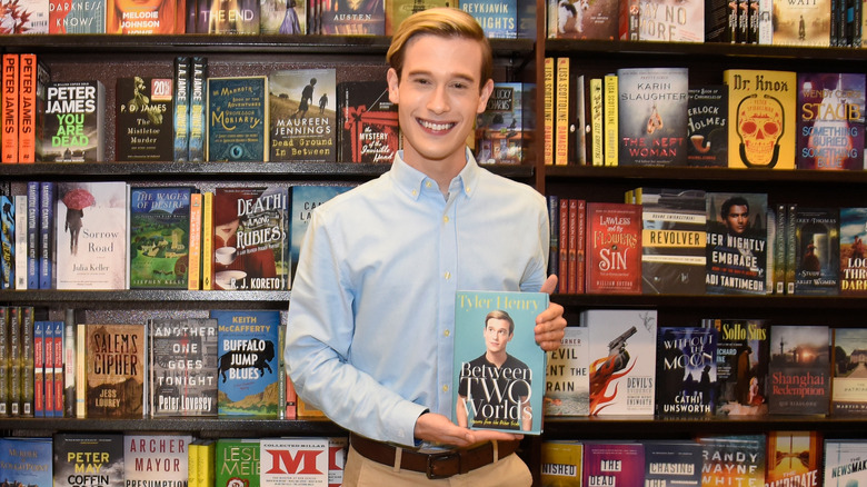 Tyler Henry shows off his book in front of a bookshelf