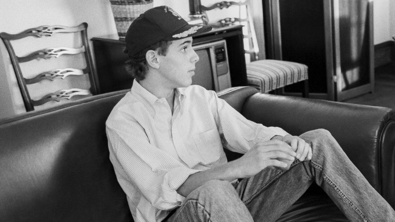 A teenage Hunter Biden sitting on a couch wearing baseball hat, shirt, and jeans with his feet on a coffee table