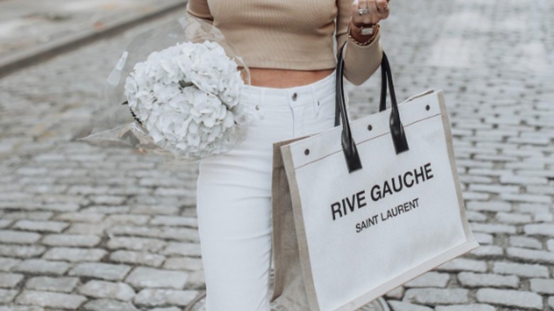 woman carrying YSL Rive Gauche bag and flowers