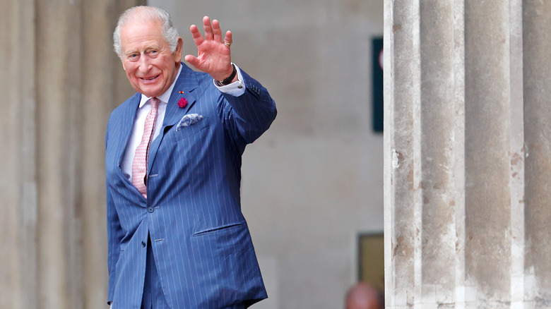 A smiling King Charles waving at the camera in a blue striped suit