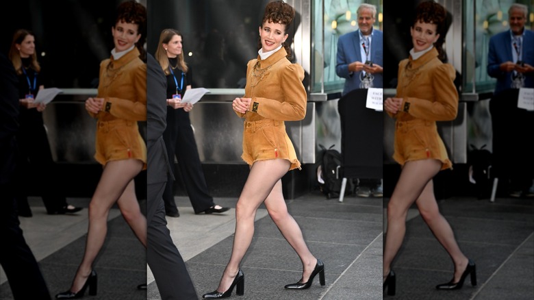 Miranda July outside gala venue wearing very short tan short with puffy-sleeve Victorian-style jacket