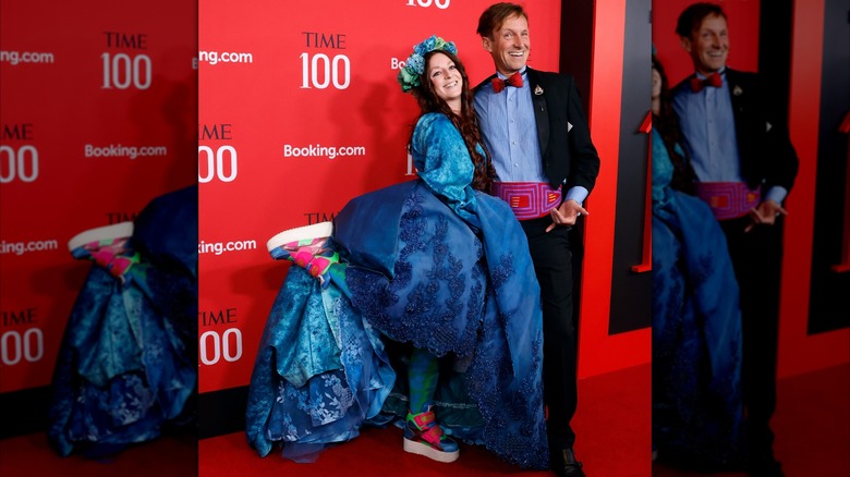 Tricia Storie with leg kicked up showing off bright sneakers under puffy dress, next to Bennett Dorrance in blue shirt, red bow-tie, and embroidered cumberbun
