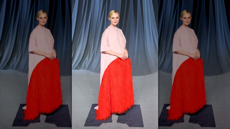Elle Fanning in a red and pink dress with a blue backdrop