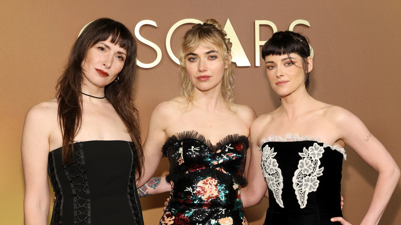 Kristen Steward, Maggie Mclean, and Imogen Poots standing together in front of an Oscars sign.