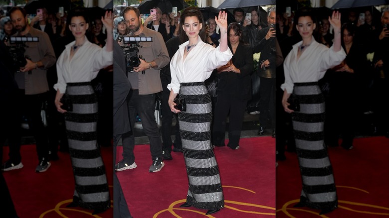 Anne Hathaway waves wearing a white shirt and striped skirt