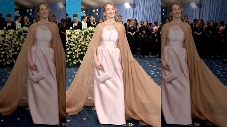 Maya Hawke poses in pink dress with tan cape