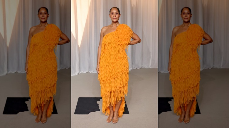 Tracee Ellis Ross poses with one hand on her hip in an orange dress