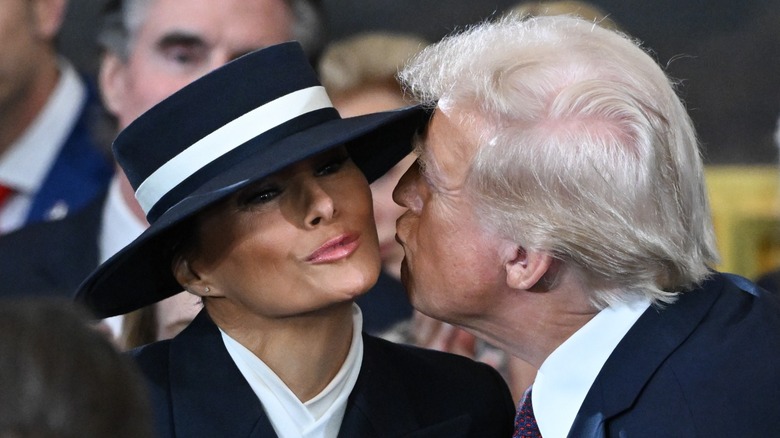 Donald Trump attempting to kiss Melania Trump's cheek under her wide-brimmed hat at his 2025 inauguration