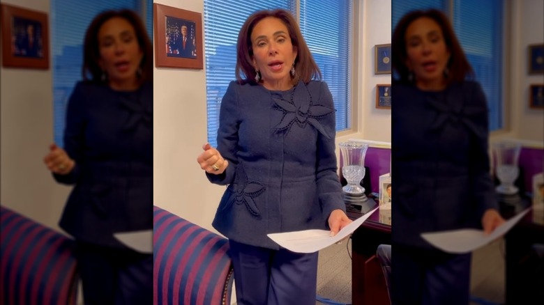 Jeanine Pirro wearing a purple jacket with orchid appliques and purple pants in her office.
