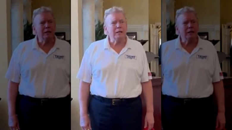 Still screenshot image of Donald Trump sporting a mullet hairstyle while wearing a white polo top and dark pants