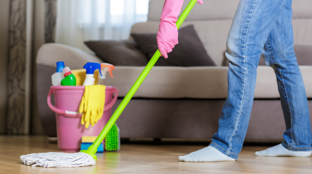 Woman wearing pink gloves mops wood floor in front of a couch.