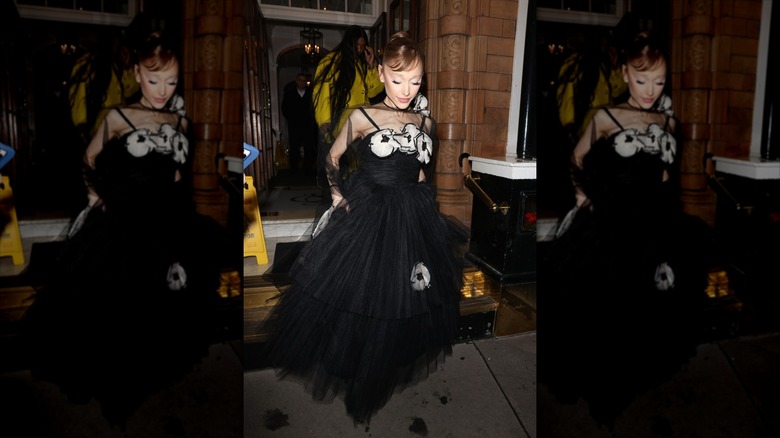 Ariana Grande in a black dress, walking onto the sidewalk.