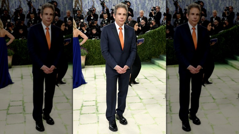 Ben Stiller posing in a dark blue suit and orange tie.