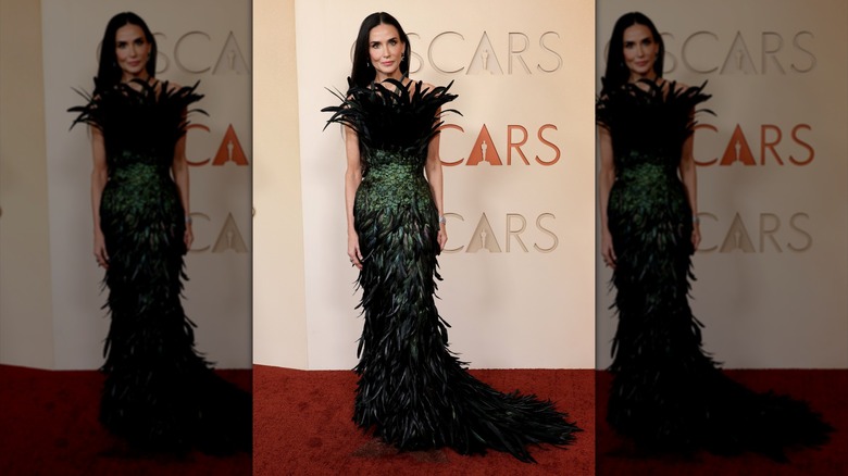 Demi Moore posing in a green and black feathered gown.