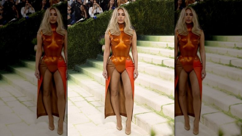 Kim Kardashian posing in a shiny, hard orange bodysuit with a skirt in the back.