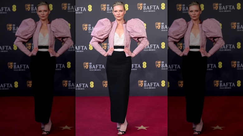 Kirsten Dunst posing in a black skirt and pink jacket with leg-of-mutton sleeves.