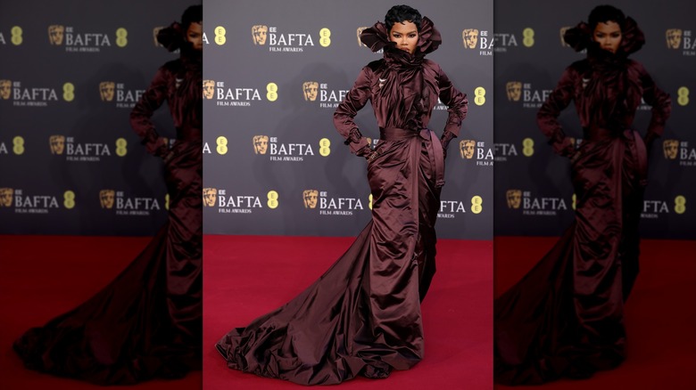 Teyana Taylor posing in a brown satin dress with a ruffled collar that extends above her ears.