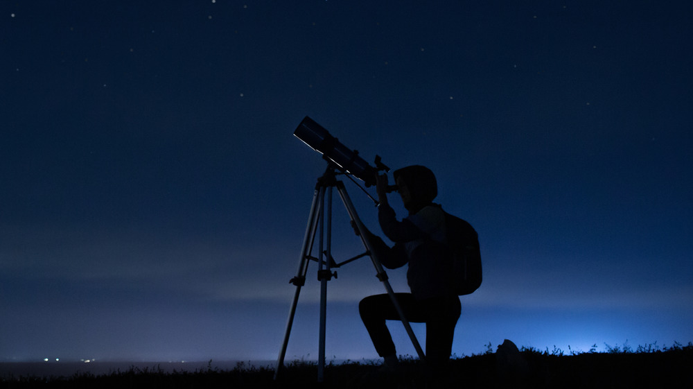A person looks through a telescope at the night sky