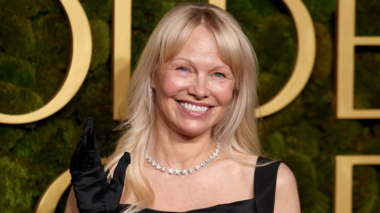 Pamela Anderson smiling while posing on the red carpet in a black dress