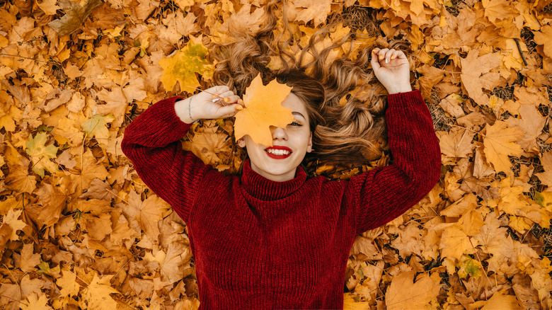 Woman in a sweater lays in a pile of leaves