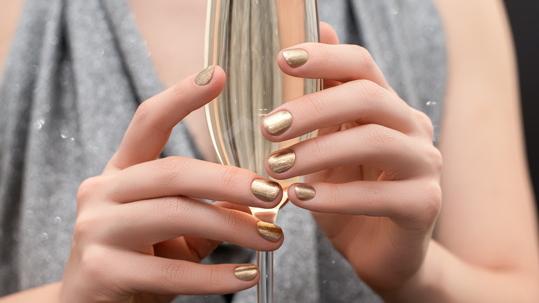A woman with gold nail polish holding a glass of champagne