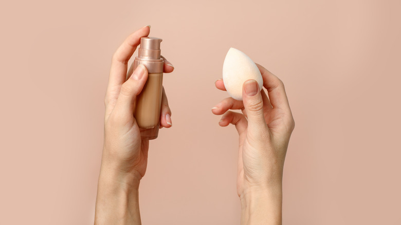 Hands hold a foundation bottle and sponge blender