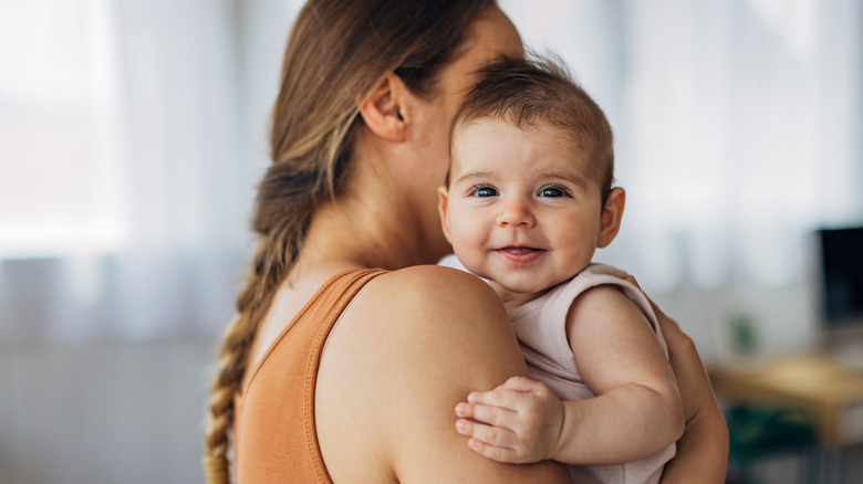 A woman holding a baby, who's looking over her shoulder