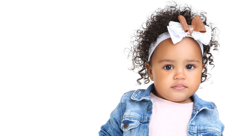 A baby girl wearing a headband with a white bow and a brown bow