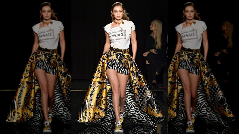 Gigi Hadid on the Versace runway wearing logo shirt and zebra shorts with long skirt