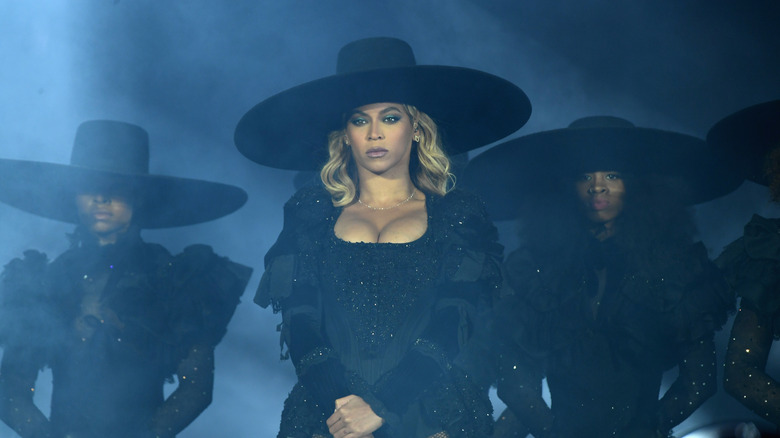 Beyonce performing on stage wearing all black and a large hat
