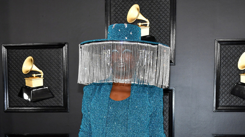 Billy Porter on red caret with large hat and fringe covering his face
