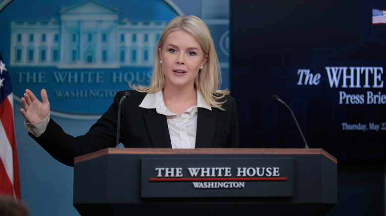 Karoline Leavitt holding a press conference in a black blazer and a white blouse