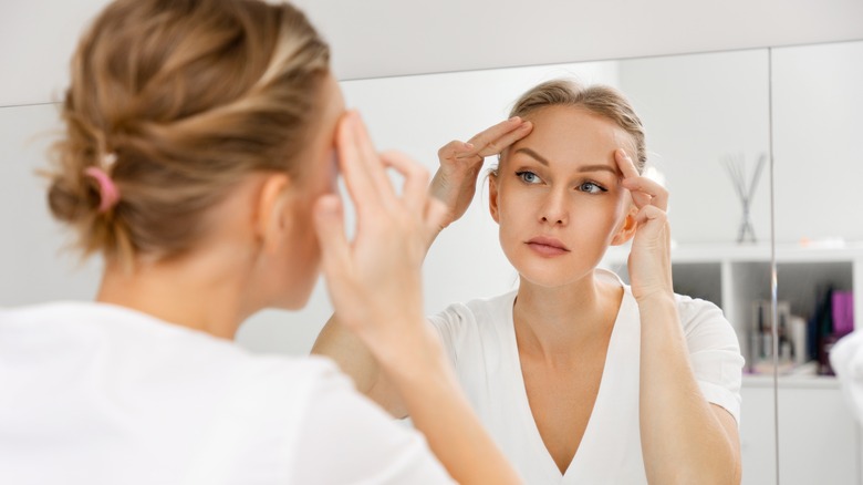 Woman looking at her forehead in mirror