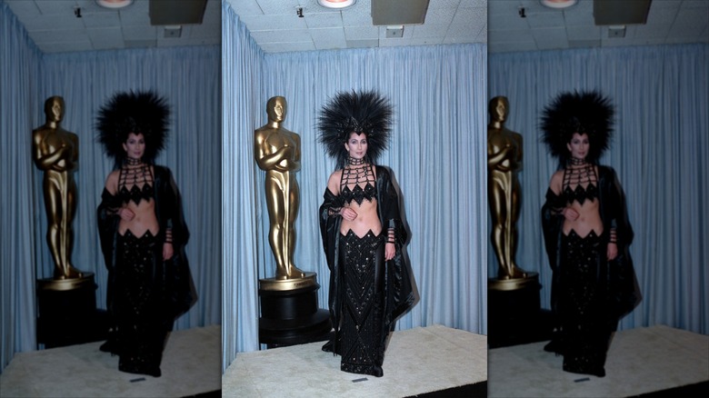 Cher posing next to a large Oscars statue in 1986