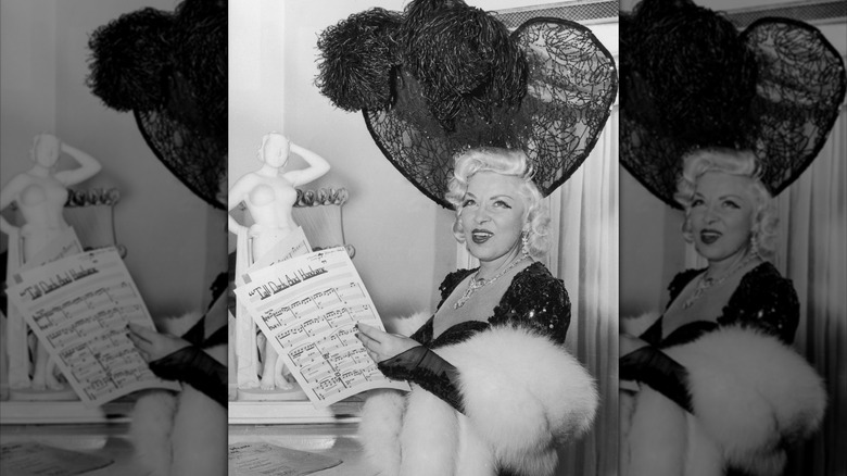 Mae West holding up sheet music while wearing elaborate furs and hat
