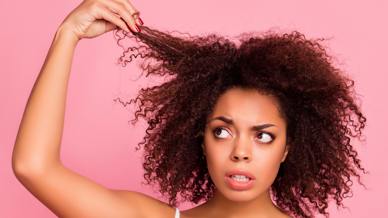 Unhappy woman pulling strands of her brunette curls up.